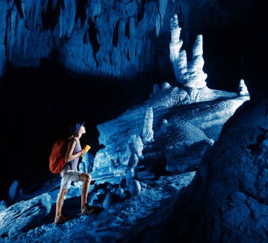 Young woman with backpack exploring huge cave with torch clipart