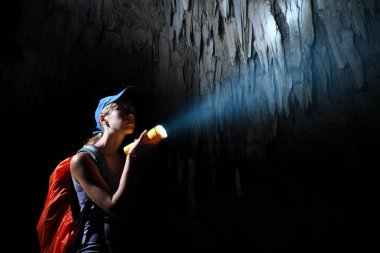 Young woman with backpack exploring cave with torch clipart
