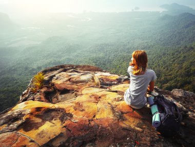 Genç bir kadın kayanın üzerinde oturuyor.