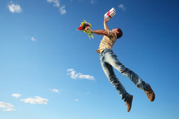 蓝蓝的天空背景上用鲜花和礼品盒跳跃的年轻人 — 图库照片