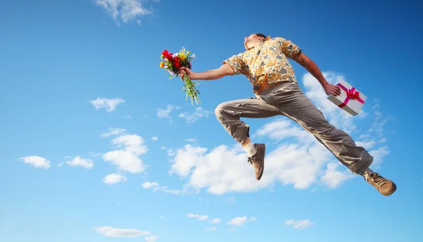 Homem pulando com flores e caixa de presente — Fotografia de Stock