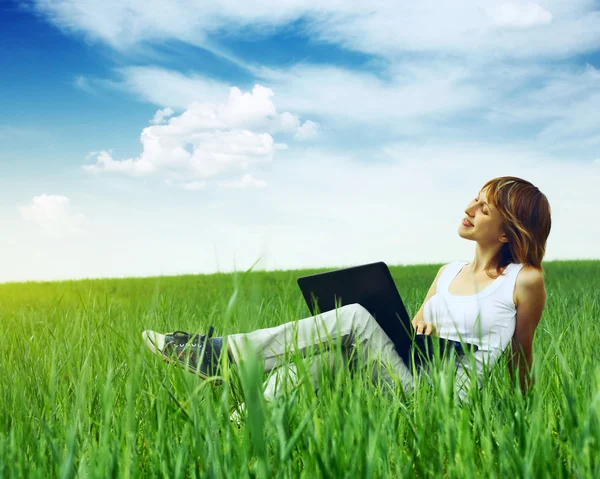 Женщина с ноутбуком сидит на зеленой траве — стоковое фото