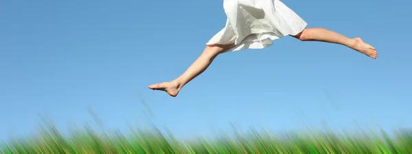 Жінка в білому платті стрибає над зеленою розмитою травою — стокове фото