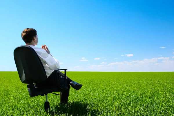 緑の牧草地で椅子に座っている若い男 — ストック写真