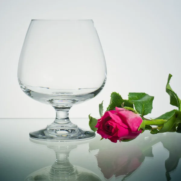 Порожнє бренді скло і рожева троянда на склі — стокове фото