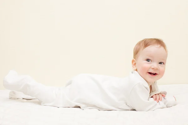 Happy smiling baby boy in white clothes is lying on sofa — Stock Photo, Image