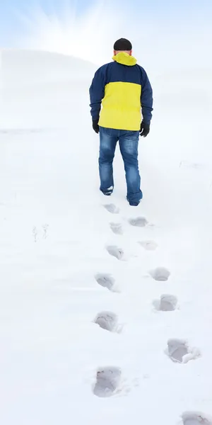 Man in gele jas lopen op sneeuw, voetafdrukken in sneeuw, achter — Stockfoto
