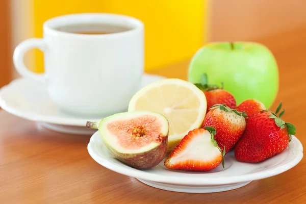 Tasse Tee, Apfel, Zitrone, Feige und Erdbeeren auf einem Teller — Stockfoto