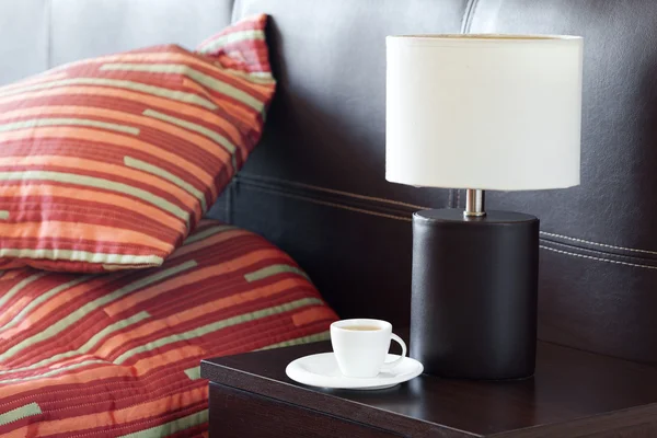 Letto con cuscino, una tazza di tè sul comodino e lampada — Foto Stock