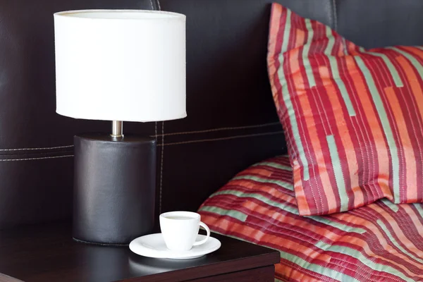 枕とベッド、ベッドサイド テーブル、ランプにお茶を一杯 — ストック写真