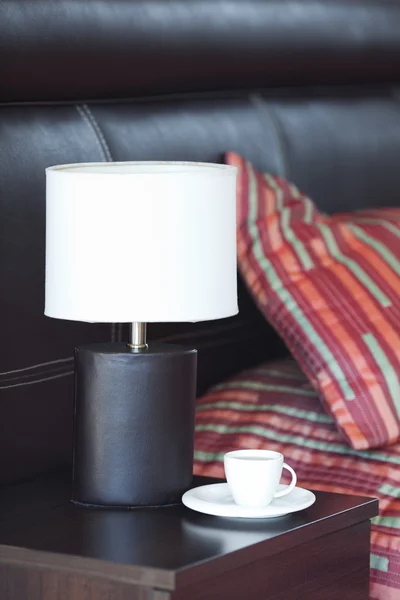 Cama com um travesseiro, uma xícara de chá na mesa de cabeceira e lâmpada — Fotografia de Stock