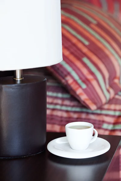 Postel s polštáři, šálek čaje na nočním stolku a lampa — Stock fotografie