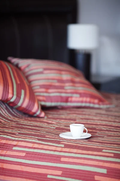 枕とベッド、ベッドサイド テーブル、ランプにお茶を一杯 — ストック写真