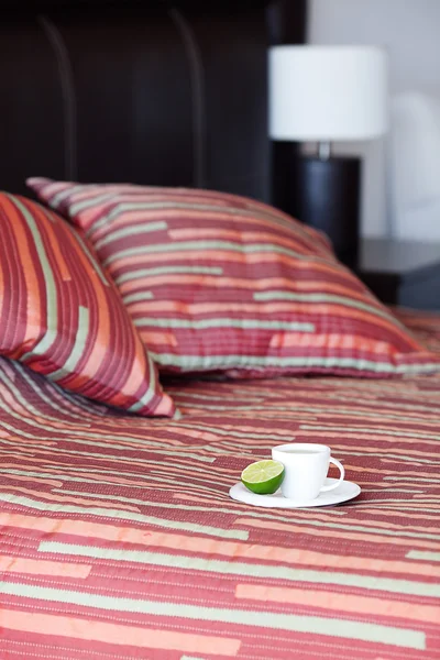 Bed met een kussen, een kopje thee op het nachtkastje en lamp — Stockfoto