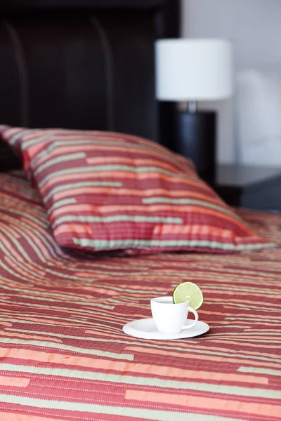 床上用枕头、 一杯茶上的床头桌和灯 — 图库照片