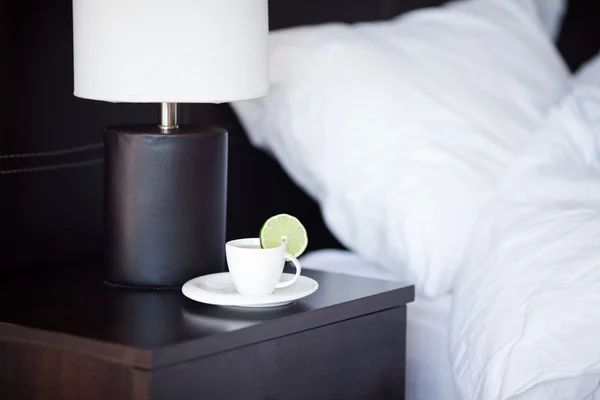 Ліжко з подушкою, чашка чаю на тумбочці та лампа — стокове фото