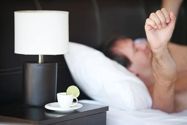 Проснувшийся мужчина и чашка чая на тумбочке и лампа — стоковое фото