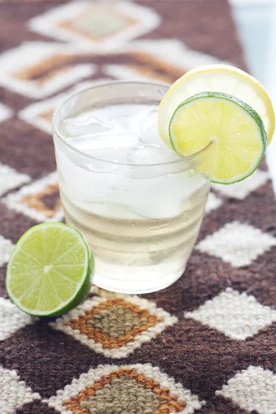 Вода с лимоном и лаймом в стакане со льдом на этническом коврике — стоковое фото