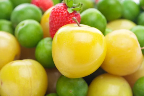 Tło zielone i żółte śliwki i truskawki — Zdjęcie stockowe