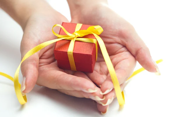 Rote Geschenkschachtel mit einer gelben Schleife in den Händen von Frauen — Stockfoto