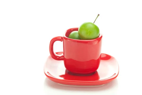Grüne Pflaume in der roten Tasse isoliert auf weiß — Stockfoto