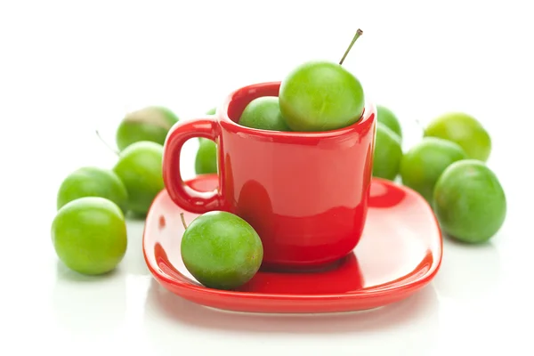 Ameixa verde no copo vermelho isolado em branco — Fotografia de Stock