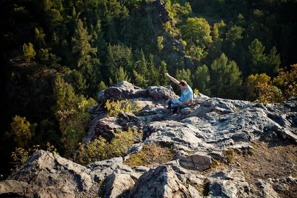 Молодой человек с ноутбуком, сидящий на скальном склоне — стоковое фото