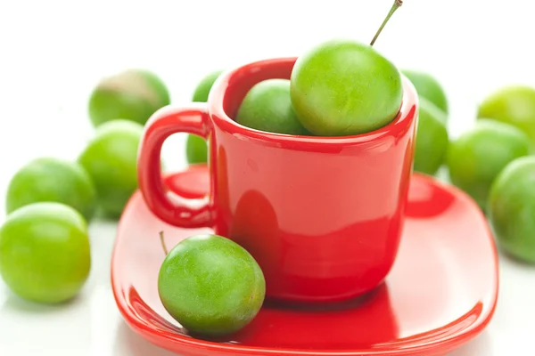 Gröna plommon i röda cup isolerad på vit — Stockfoto