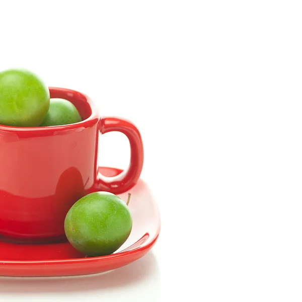 Gröna plommon i röda cup isolerad på vit — Stockfoto