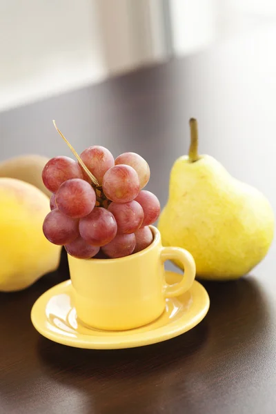 Pesca, pera, uva in una tazza e piattino su un tavolo di legno — Foto Stock