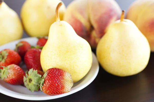 Strawberry in plate, pear and peach on a wooden table — Stock Photo, Image