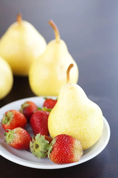 Strawberry in plate and pear on a wooden table — Stock Photo, Image
