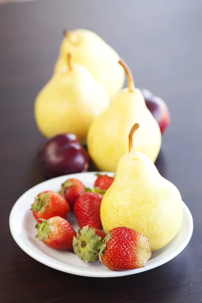 Fragola in piatto, uva e pera su un tavolo di legno — Foto Stock