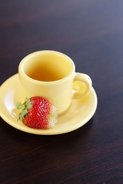 Jordgubbar och en kopp med fat på ett träbord — Stockfoto