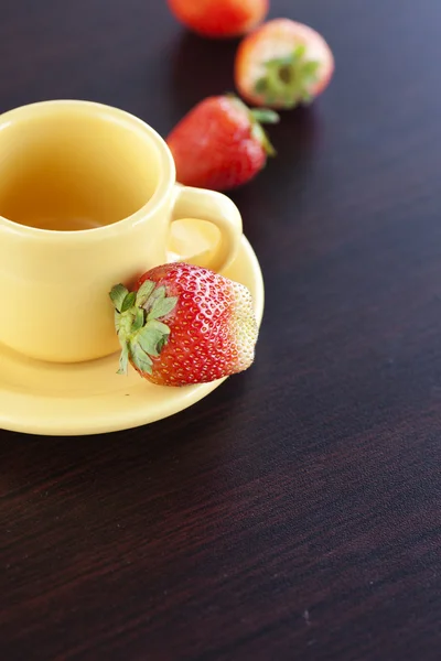 Erdbeeren und eine Tasse mit Untertasse auf einem Holztisch — Stockfoto