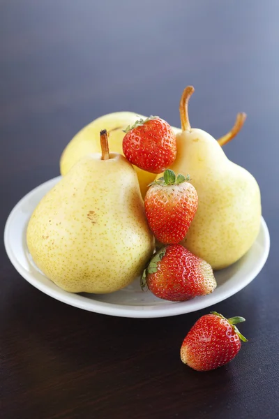 Jordgubbar och päron på en tavla på ett träbord — Stockfoto