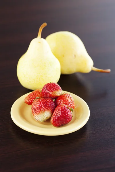 Erdbeeren und Birnen auf einem Teller auf einem Holztisch — Stockfoto