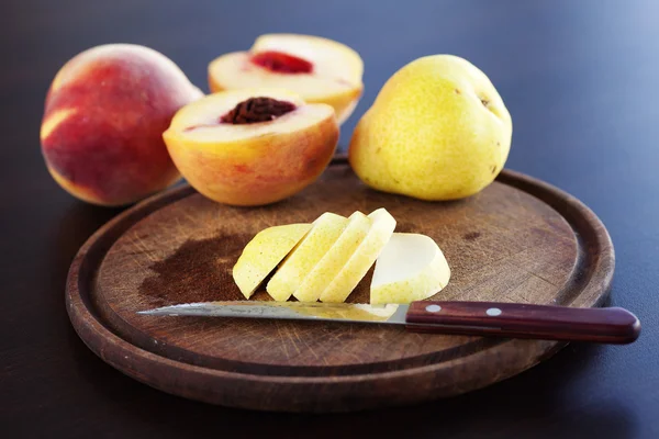 Persika, päron och en kniv på en skärbräda — Stockfoto