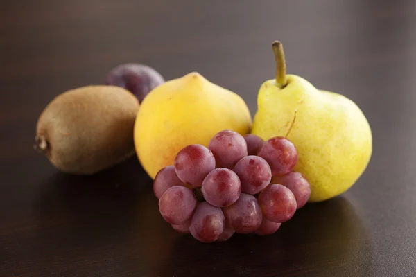 Perzik, peer, kiwi en druiven liggend op een houten tafel — Stockfoto