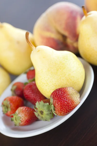 Jordgubbar i plattan, päron och persikor på ett träbord — Stockfoto