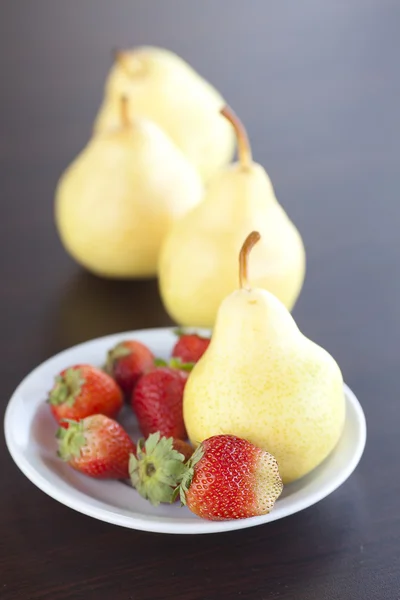 Jordgubbar i plattan, päron och persikor på ett träbord — Stockfoto