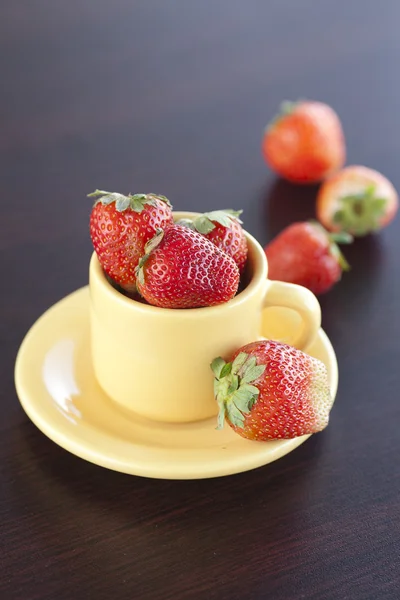 Aardbeien en een kop met schotel op een houten tafel — Stockfoto