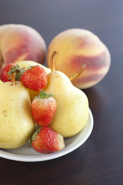 Mansikka lautasella, päärynä ja persikka puinen pöytä — kuvapankkivalokuva