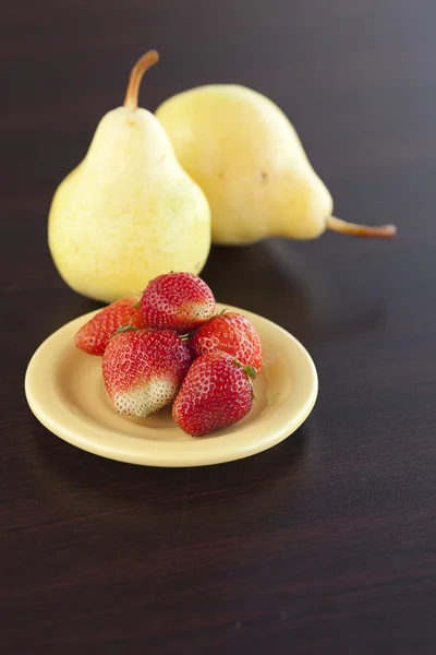 La fresa en el plato y la pera sobre la mesa de madera — Foto de Stock