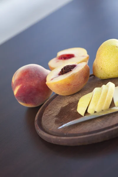 Persikka, päärynä ja veitsi leikkuulaudalla — kuvapankkivalokuva