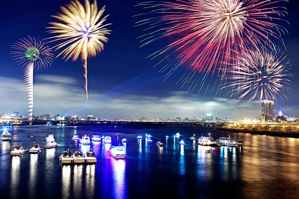 stock image Fireworks firing up into the sky with a boat on a river below them, with a