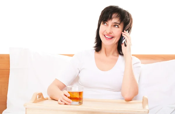 Mujer en la cama hablando por teléfono con vidrio sobre jugo en bandeja —  Fotos de Stock