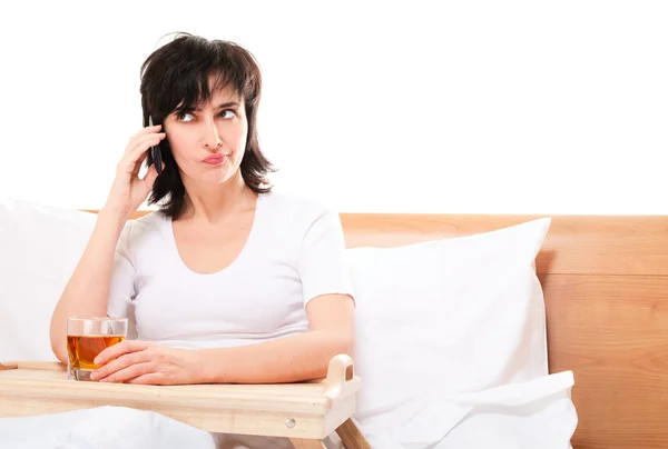 Kobieta w łóżku rozmawia przez telefon ze szkłem sok na tacy — Zdjęcie stockowe