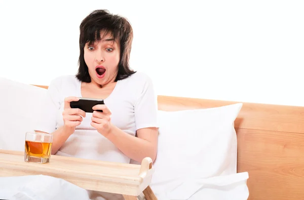 女性はベッドの中で携帯電話でビデオゲームを再生します。 — ストック写真