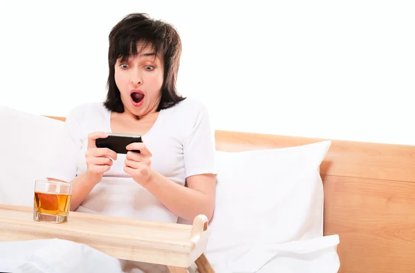 Vrouw speelt video games op mobiele telefoon in bed — Stockfoto